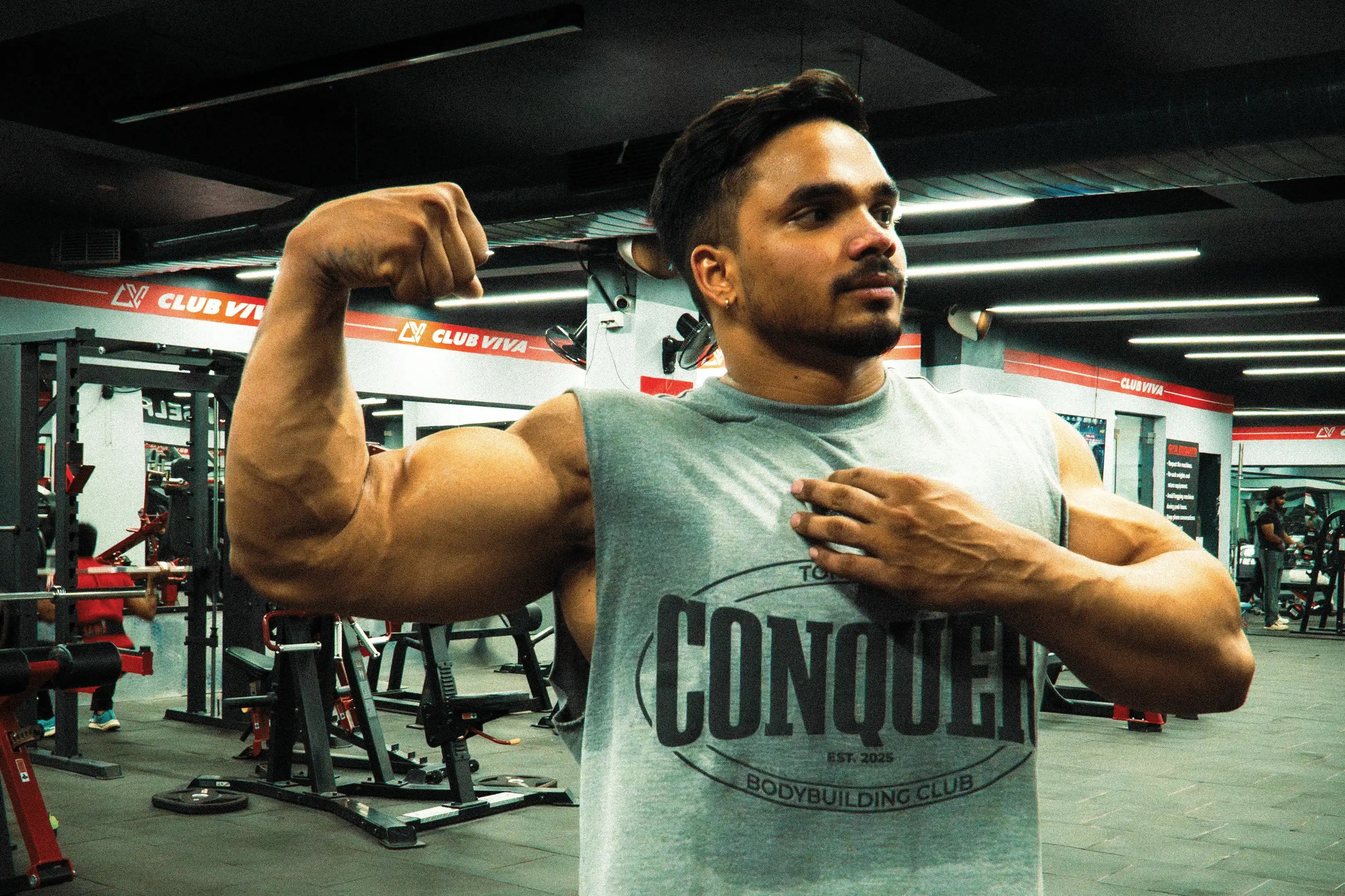 Muscular man wearing sleeveless gym shirt flexing bicep in modern fitness center