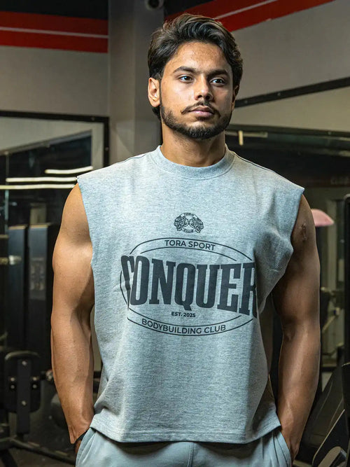 Man in gym wearing sleeveless grey muscle shirt with 'Conquer Bodybuilding Club' print