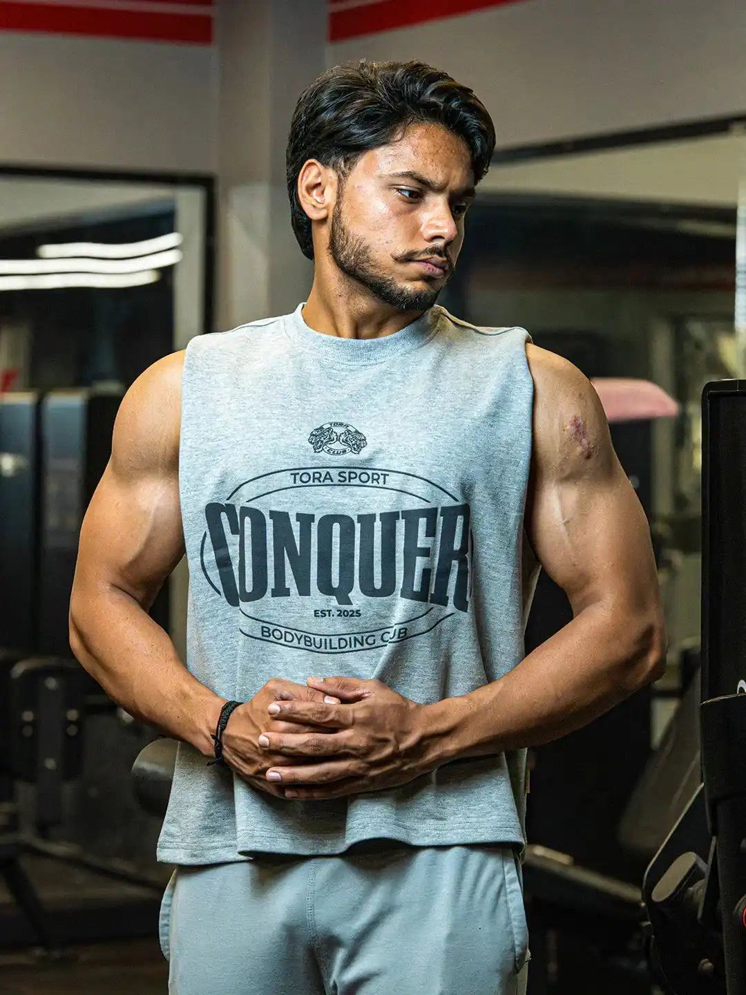Muscular man in sleeveless grey CONQUER gym shirt posing in fitness center