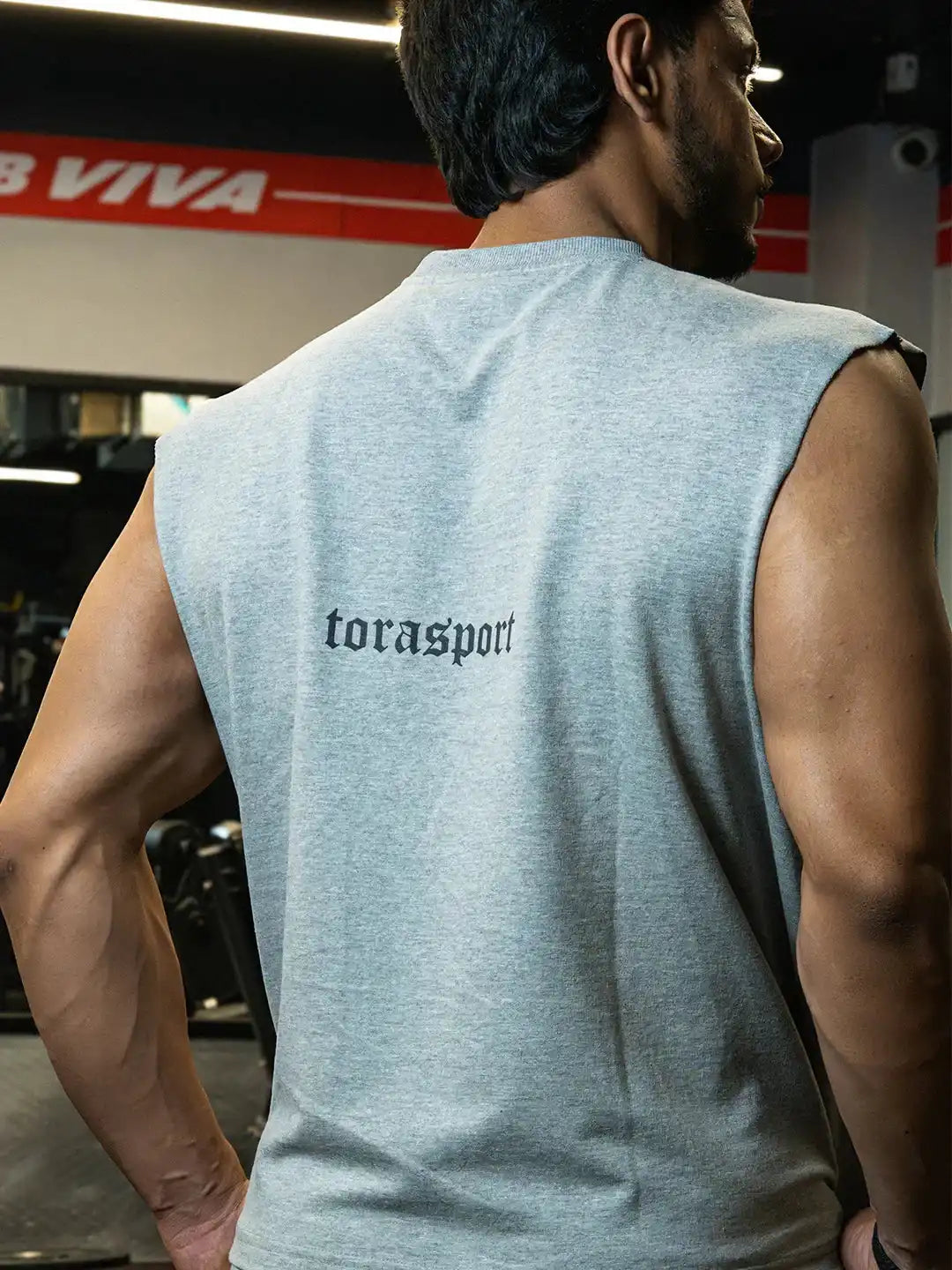 Man in gym wearing sleeveless grey shirt with 'torasport' text on back