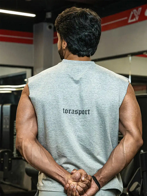 Muscular man in sleeveless grey gym shirt with 'torasport' text, standing in gym