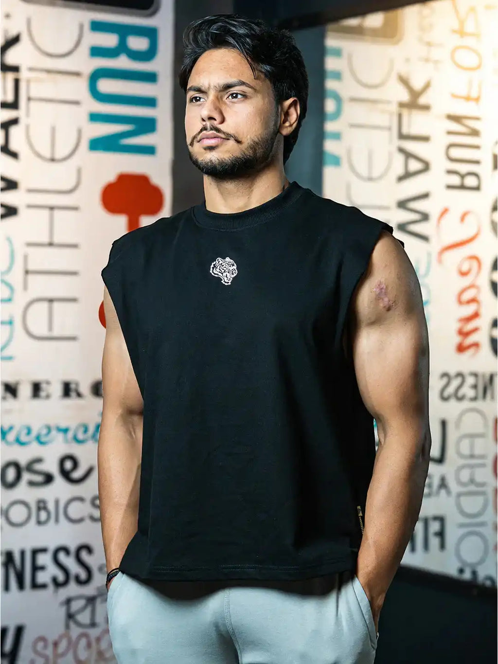 Athletic man modeling black sleeveless gym shirt and light pants in a fitness center