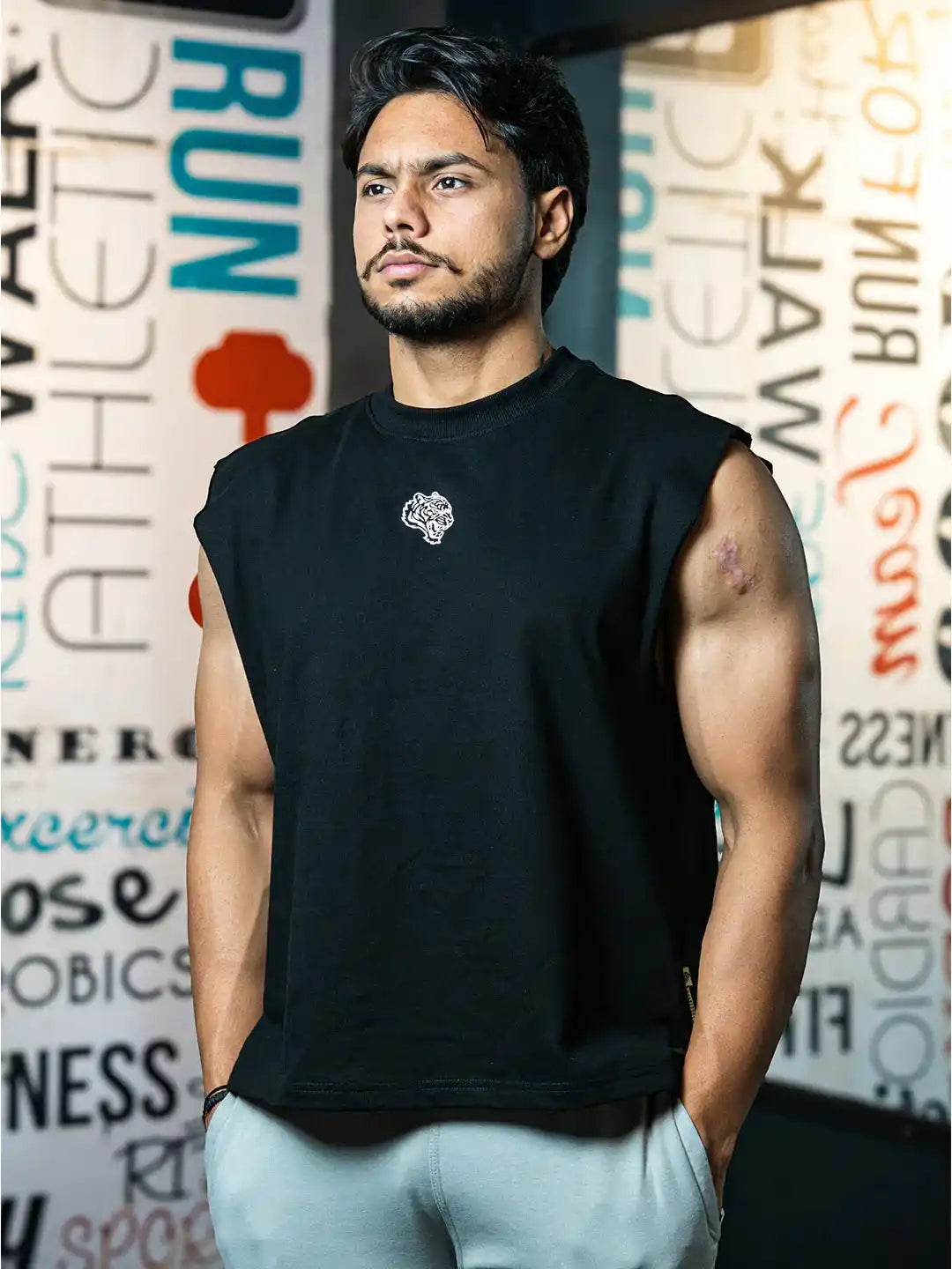 Athletic man modeling black sleeveless gym shirt and light pants in a fitness center