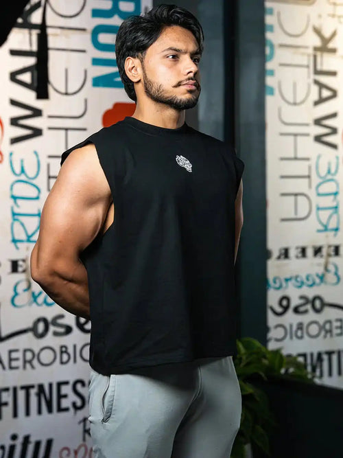 Athletic man in black sleeveless gym shirt and light joggers standing in fitness studio