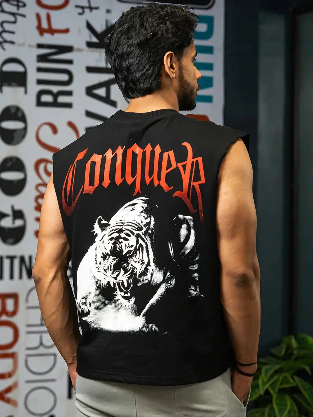 Man wearing sleeveless gym shirt with fierce tiger graphic and 'Conquer' text, fitness wall art