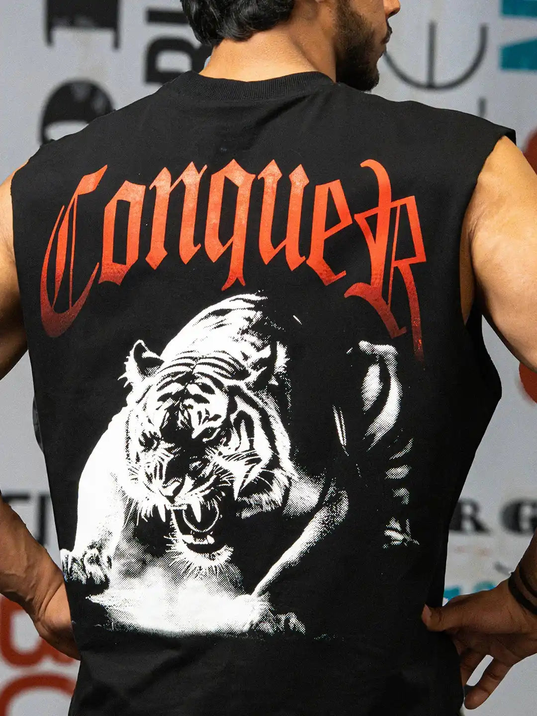 Man wearing black gym tank top with bold 'Conquer' text and graphic roaring tiger.