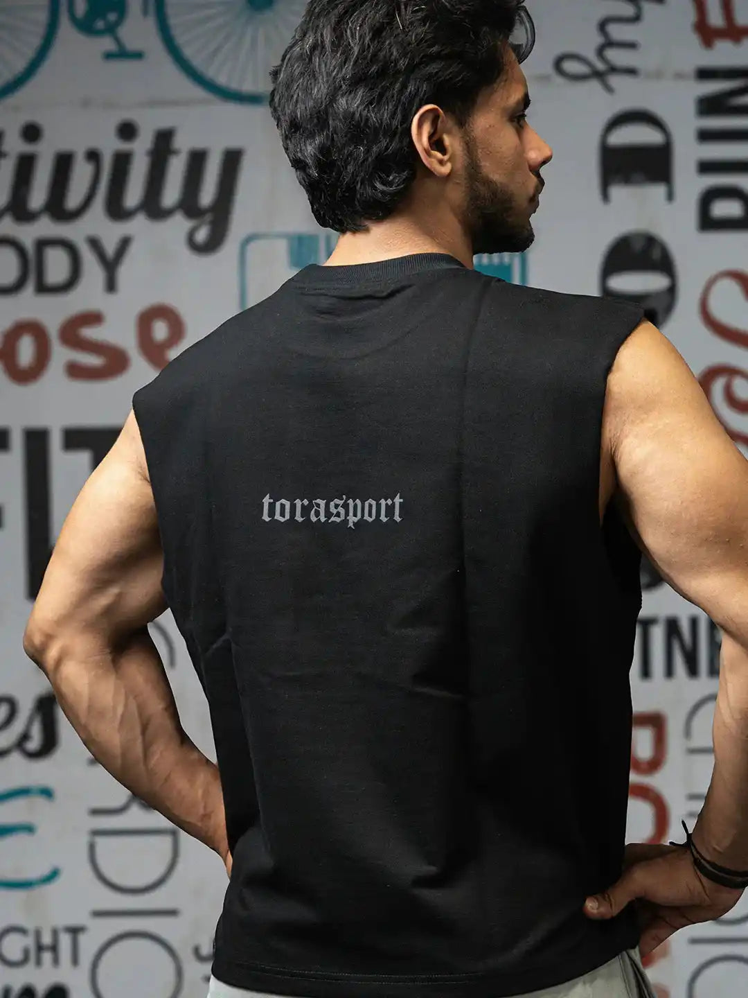 Man wearing sleeveless black gym shirt with 'torasport' text, athletic fit, gym background