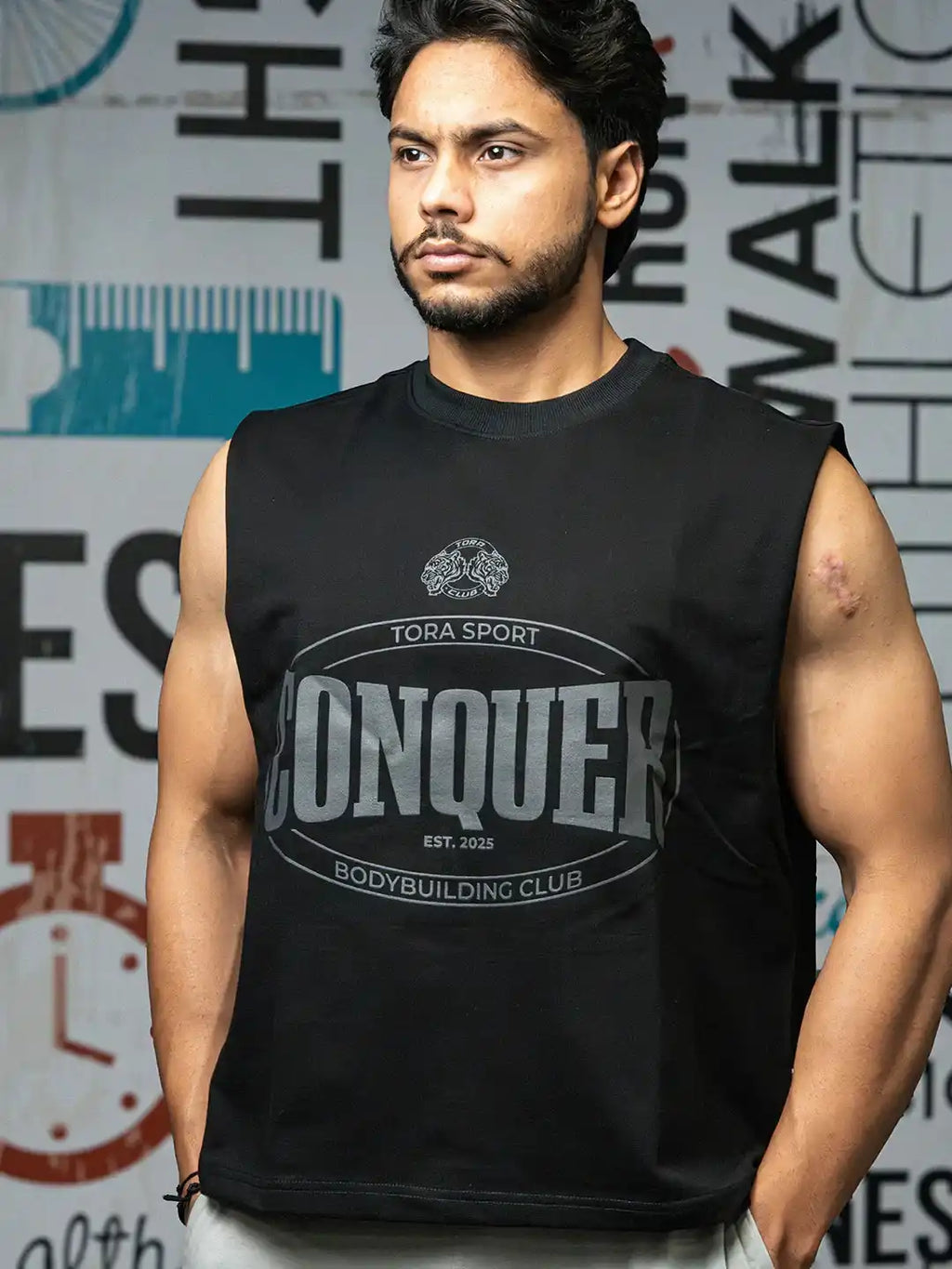 Muscular man in black sleeveless CONQUER T-shirt, gym wear, standing indoors