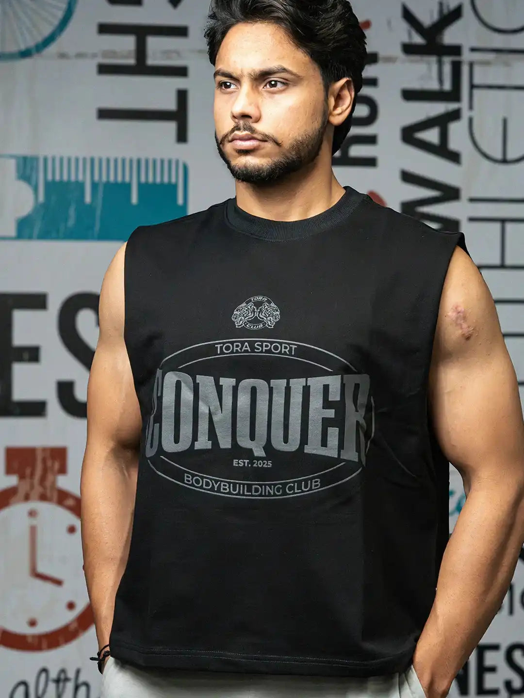 Muscular man in black sleeveless CONQUER T-shirt, gym wear, standing indoors