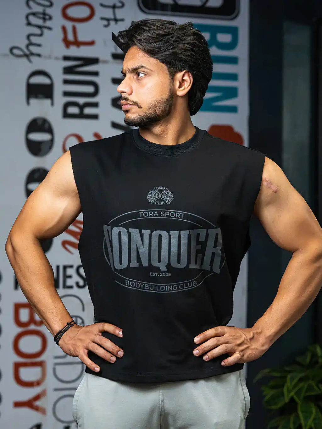 Sleeveless black gym shirt with 'Conquer' print worn by man in fitness center