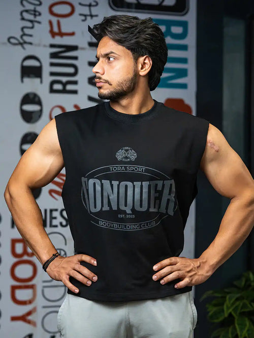 Sleeveless black gym shirt with 'Conquer' print worn by man in fitness center