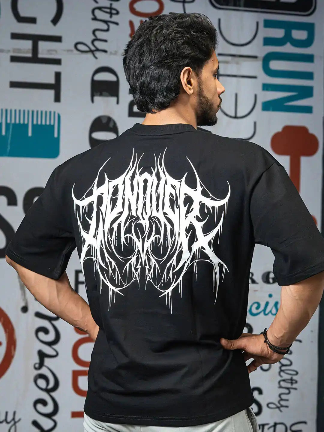 Man wearing black oversized t-shirt with bold white graphic print on back, indoor gym setting