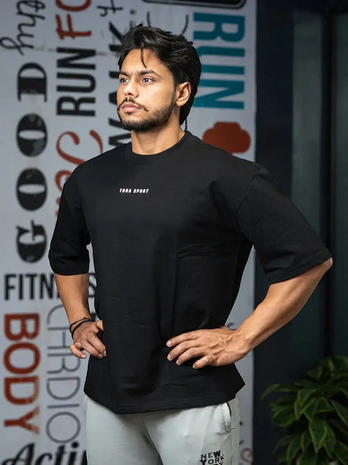 Man in black oversized gym t-shirt and grey sweatpants posing in active lifestyle setting