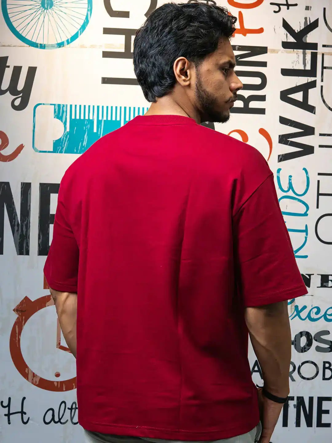 Man wearing a plain red gym t-shirt standing in front of fitness-themed wall art