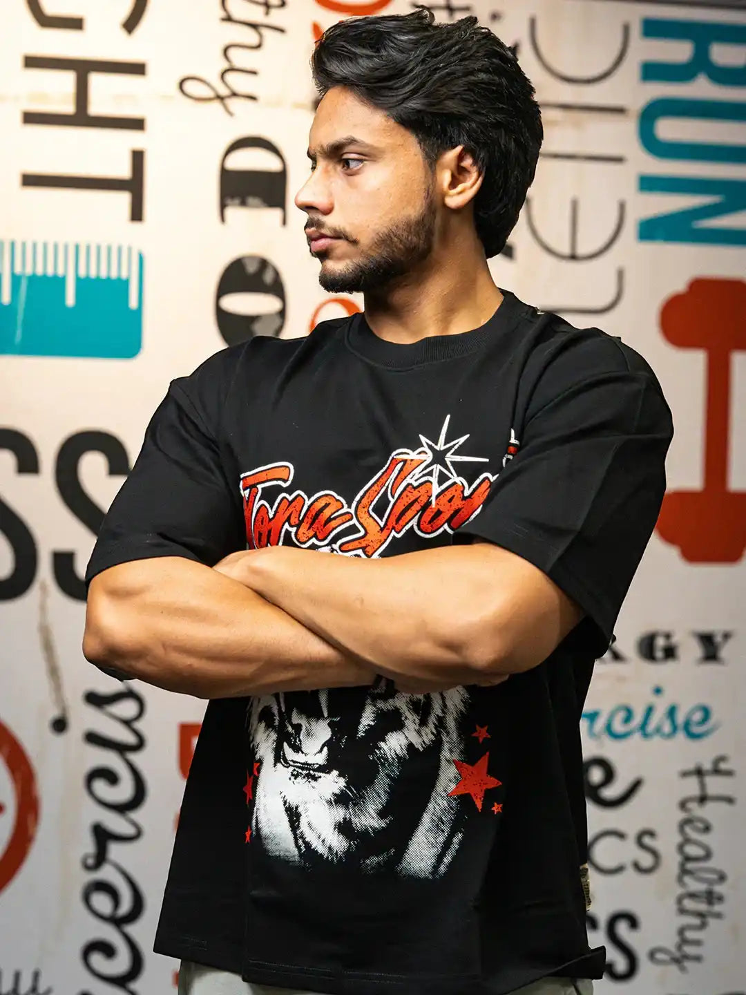 Man in black gym t-shirt with graphic tiger print and red stars, standing arms crossed