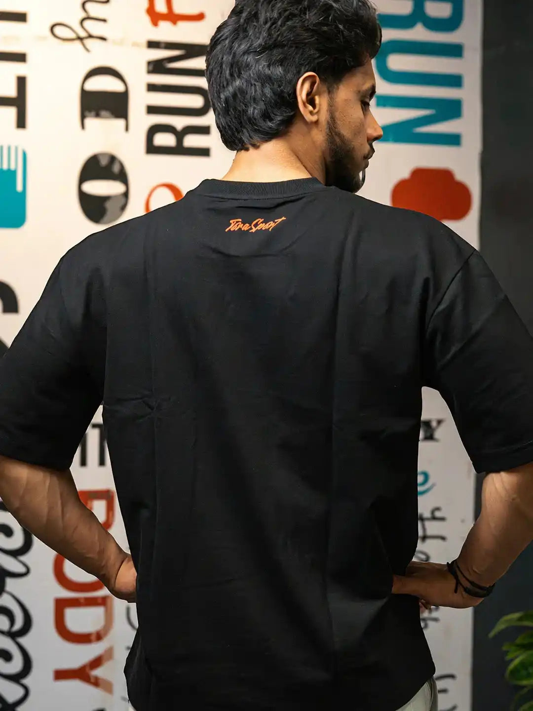 Man wearing black gym t-shirt with lettering on back, standing in front of wall art