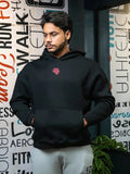Man in black gym hoodie with front pocket and red logo, standing indoors by motivational wall.